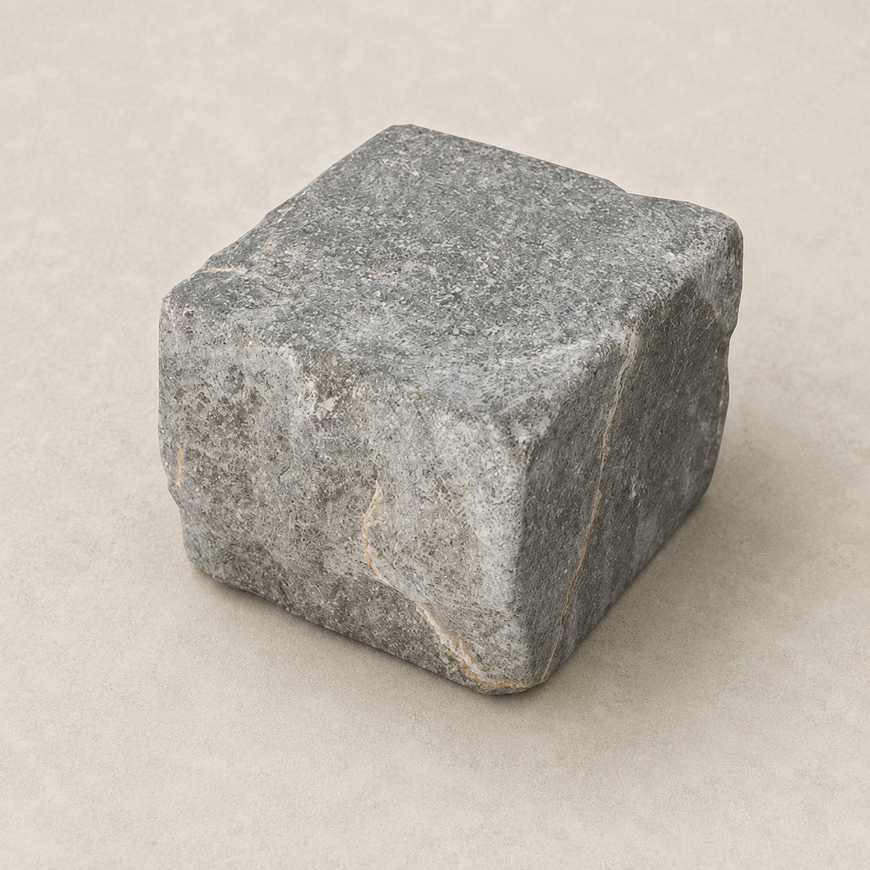 Le Pavé de 2068 : pavé cubique gris aux arêtes usées, posé sur fond beige.